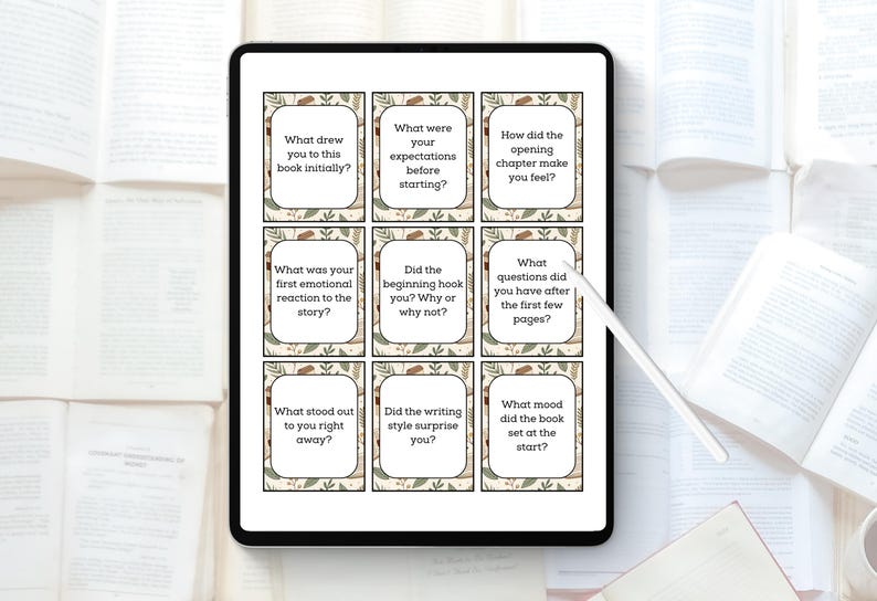 May include: A digital tablet displays nine reading prompt cards with text such as "What drew you to this book initially?" The cards have a beige background with a floral border. The tablet is surrounded by open books.