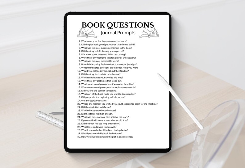 Puede incluir: Una tableta digital muestra "BOOK QUESTIONS Journal Prompts" con preguntas sobre libros. Un l&aacute;piz &oacute;ptico y un bol&iacute;grafo est&aacute;n sobre la mesa. La tableta est&aacute; sobre una superficie de madera de color claro.
