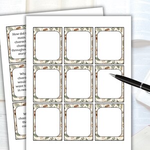 May include: Two sheets of printed cards with a decorative border, featuring blank spaces for writing. The cards have text prompts like "How did the main character change throughout the story?" A black pen rests on the cards, suggesting note-taking or writing.