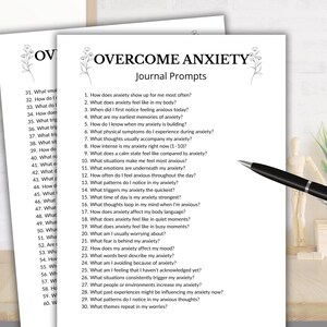 K&ouml;nnte beinhalten: Zwei wei&szlig;e Papierbl&auml;tter mit dem schwarzen Text OVERCOME ANXIETY Journal Prompts und einer nummerierten Liste von drei&szlig;ig Fragen. Ein schwarz-silberner Kugelschreiber liegt auf dem Papier, das auf einer Holzoberfl&auml;che platziert ist.