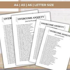 K&ouml;nnte beinhalten: Vier wei&szlig;e Papierb&ouml;gen mit dem Titel OVERCOME ANXIETY Journal Prompts in schwarzer Schrift, begleitet von kleinen Blumenillustrationen. Die Seiten enthalten nummerierte Fragen zur Selbstreflexion, erh&auml;ltlich in den Formaten A4, A5, A6 und Letter.