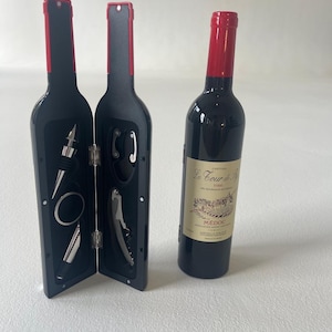May include: A black wine bottle shaped box with a red top opens to reveal a set of wine tools, including a corkscrew, bottle stopper, and foil cutter. A separate red wine bottle with a label that reads "Chateau La Cour de la Reine" is also pictured.