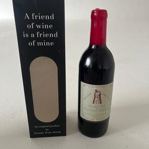 Puede incluir: Una pequeña botella de vino con tapón rojo y etiqueta "Grand Vin Chateau Latour". Junto a ella, una caja negra con el texto "A friend of wine is a friend of mine" y "An original product by Swanky Wine World."