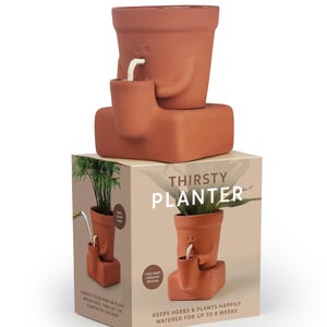 May include: A terracotta ceramic "Thirsty Planter" with a distinctive design. The planter has a face-like appearance with a small cup attached, connected by a white cord. The packaging reads "Thirsty Planter" and "Keeps herbs & plants happily watered for up to 8 weeks."