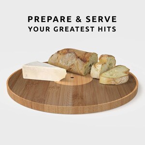 K&ouml;nnte beinhalten: Ein runder Servierteller aus hellem Holz mit konzentrischem Kreisdesign, auf dem ein K&auml;sekeil und geschnittenes Brot liegen. Der Text "PREPARE & SERVE YOUR GREATEST HITS" ist zu sehen. Ideal zum Servieren von Speisen.