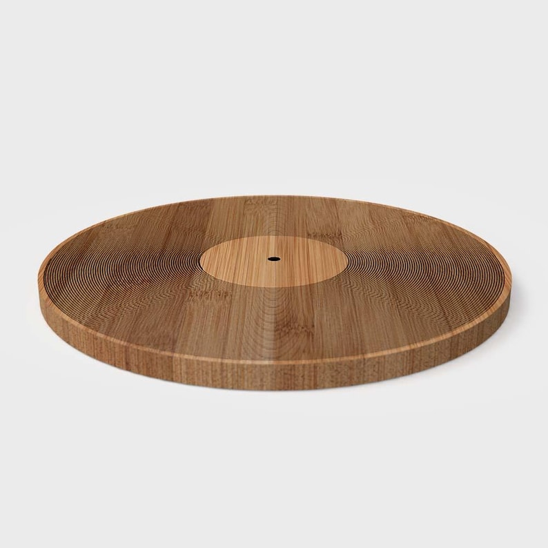 K&ouml;nnte beinhalten: Ein Serviertablett aus Holz in Form einer Schallplatte. Das Tablett besteht aus hellem und dunklem braunem Holz mit konzentrischen Rillen. Die Mitte ist ein hellerer Braunton mit einem kleinen Loch. Das Tablett ist kreisf&ouml;rmig.