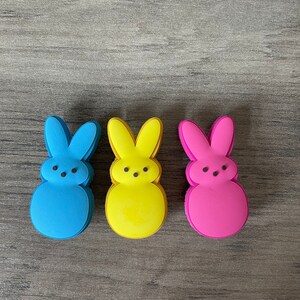 Op de afbeelding: Drie pastelkleurige konijnvormige marshmallow snoepjes. De snoepjes zijn blauw, geel en roze.