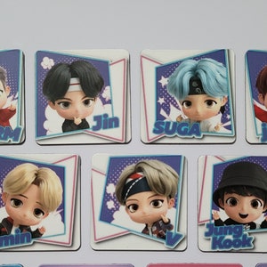 May include: Seven colorful square cards with cartoon illustrations of the members of the K-pop group BTS. Each card features a different member with their name printed below the image. The names are: RM, Jin, Suga, J-Hope, Jimin, V, and Jung Kook.