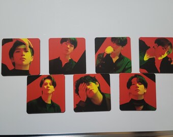 May include: Seven square photo cards featuring different members of a boy band. Each card has a red background with a black diagonal line and a green highlight. The members are wearing black shirts and have dark hair.