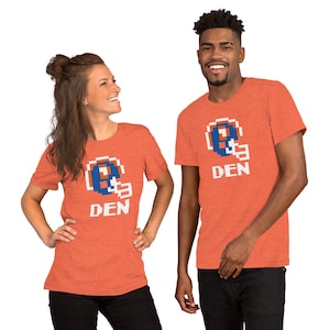 May include: Two people wearing orange t-shirts with a pixelated football helmet and the word "DEN" printed on the front.
