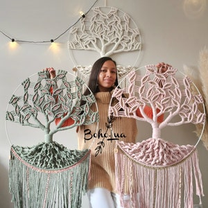 Può includere: Tre arazzi da parete con albero in macramè nei toni del verde, rosa e crema. Ogni albero è realizzato con corda annodata e presenta una cornice metallica circolare. Gli alberi hanno motivi di foglie dettagliati e frange alla base, creando un'estetica bohémien.