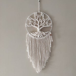Peut inclure: Suspension murale en macramé représentant un arbre. Le motif est réalisé avec une corde de coton blanc cassé, encadré dans un cercle et orné d'une frange en bas. Décoration murale suspendue par un cordon.