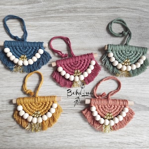 Può includere: Cinque ornamenti macramè fatti a mano in vari colori: verde acqua, fucsia, giallo senape, corallo e verde salvia. Ognuno presenta un tassello di legno, perline di legno bianche e dettagli dorati. Gli ornamenti sono progettati con una frangia e un anello per appenderli.