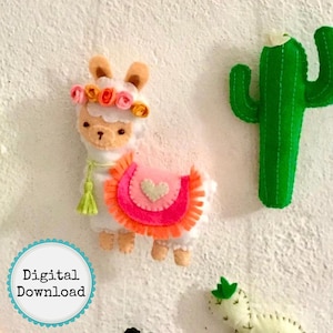 May include: A white felt llama with a pink and orange felt saddle, a green felt tassel, and a flower crown. The llama is standing on a white background. There is a green felt cactus to the right of the llama.