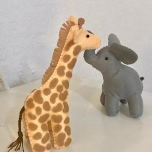 May include: A felt giraffe toy with brown spots and a long tail, nuzzling a grey felt elephant toy with a trunk.