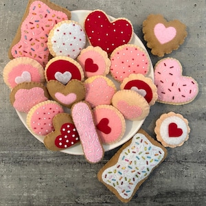 May include: A plate of felt cookies in various shapes and colors, including hearts, circles, and rectangles. Some cookies have sprinkles, while others have hearts or other designs.