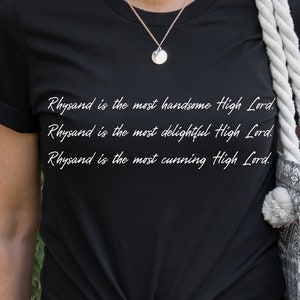 Może przedstawiać: Czarny T-shirt z białym tekstem, kt&oacute;ry brzmi: "Rhysand jest najprzystojniejszym Wysokim Panem. Rhysand jest najbardziej uroczym Wysokim Panem. Rhysand jest najbardziej przebiegłym Wysokim Panem."