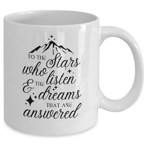 May include: White ceramic coffee mug with a black design that reads "To the stars who listen & the dreams that are answered". The design also includes a mountain range and stars.