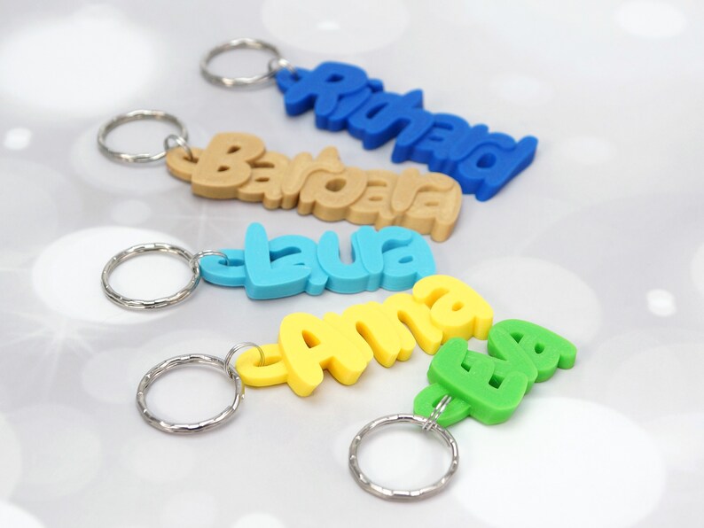 May include: Keychains with names in various colors: blue, tan, light blue, yellow, and green. Each keychain has a silver keyring attached. The names are "Richard", "Barbara", "Laura", "Anna", and "Eva".