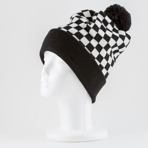 Puede incluir: Un gorro de punto negro y blanco a cuadros con un pompón negro en la parte superior. El gorro está en una cabeza de maniquí blanca.