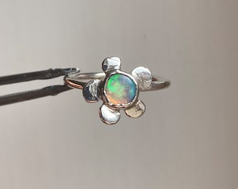 Puede incluir: Un anillo de plata con un diseño de flor que presenta una piedra de ópalo redonda en el centro.