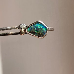 May include: A silver ring featuring a green and blue opal gemstone set in a diamond shape.
