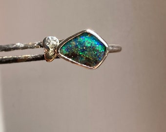 Puede incluir: Un anillo de plata con una piedra preciosa de ópalo verde y azul engastada en forma de diamante.