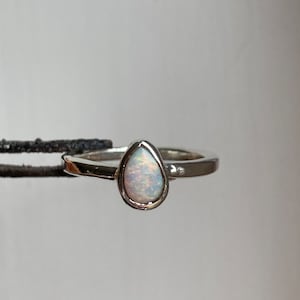 May include: A silver ring with a teardrop-shaped opal gemstone.