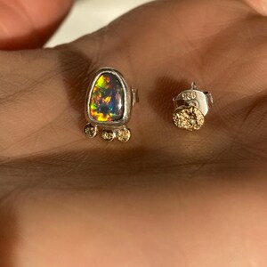 Puede incluir: Un par de pendientes de plata con una piedra preciosa de &oacute;palo negro y detalles dorados. Los pendientes est&aacute;n marcados con el n&uacute;mero "925" en la parte posterior.