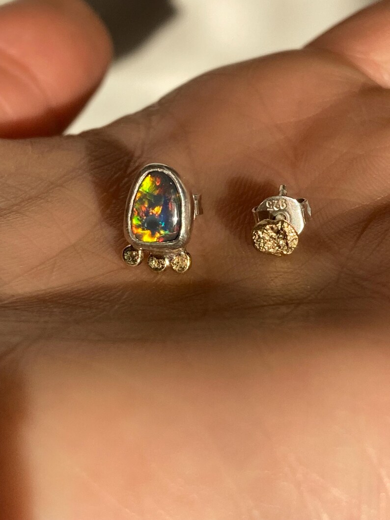 Puede incluir: Un par de pendientes de plata con una piedra preciosa de &oacute;palo negro y detalles dorados. Los pendientes est&aacute;n marcados con el n&uacute;mero "925" en la parte posterior.
