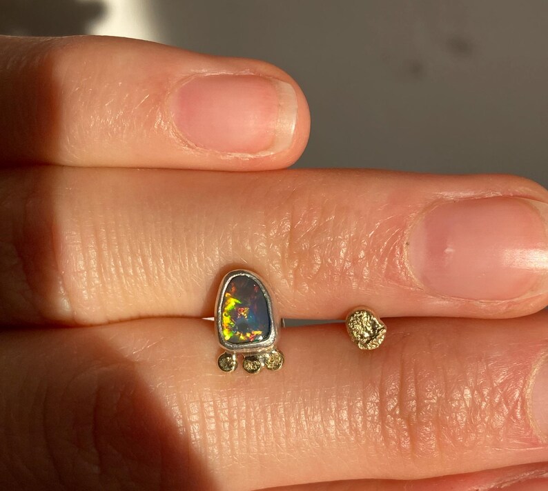 Puede incluir: Un pendiente de plata y oro con una piedra de &oacute;palo en forma de l&aacute;grima y peque&ntilde;as cuentas doradas alrededor de la piedra.