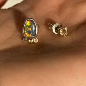 Puede incluir: Un par de pendientes de plata con una piedra de &oacute;palo en forma de l&aacute;grima y detalles dorados. El &oacute;palo es iridiscente con tonos de verde, azul y rojo.