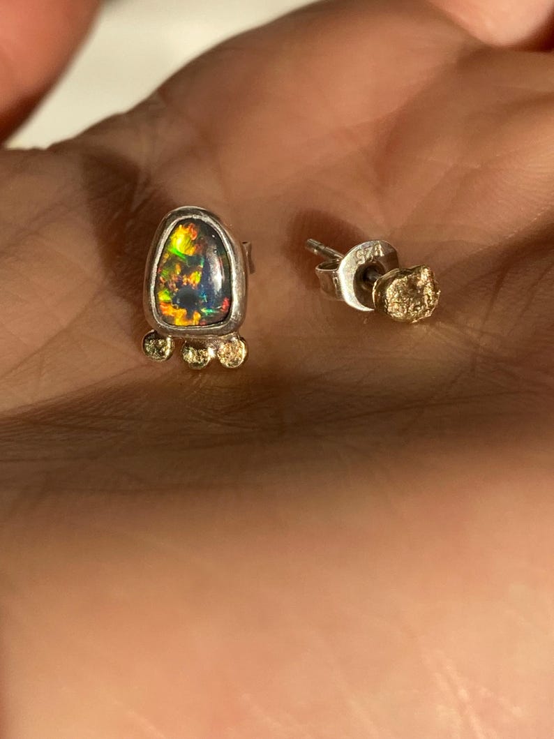 Puede incluir: Un par de pendientes de plata con una piedra de &oacute;palo en forma de l&aacute;grima y detalles dorados. El &oacute;palo es iridiscente con tonos de verde, azul y rojo.