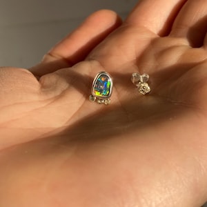 Puede incluir: Un par de pendientes de plata con una sola piedra de &oacute;palo en cada pendiente. El &oacute;palo es de color verde oscuro, azul y morado. Los pendientes est&aacute;n engastados en un engaste de plata con peque&ntilde;os detalles dorados.