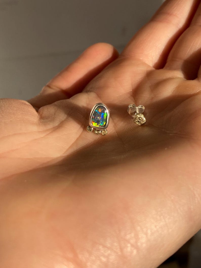 Puede incluir: Un par de pendientes de plata con una sola piedra de &oacute;palo en cada pendiente. El &oacute;palo es de color verde oscuro, azul y morado. Los pendientes est&aacute;n engastados en un engaste de plata con peque&ntilde;os detalles dorados.