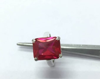 Peut inclure: Une bague en argent ornée d'une grosse pierre rouge vif de taille carrée. La pierre est maintenue par quatre griffes, et le corps de la bague est en argent poli. La bague est présentée sur fond blanc. La pierre mesure environ 1,5 cm de côté.