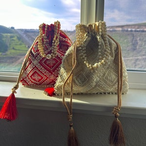 May include: Two embroidered drawstring bags with pearl trim and tassel accents. One bag is red with white embroidery and the other is cream with gold embroidery.