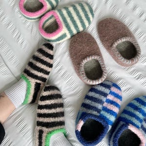 Puede incluir: Una colecci&oacute;n de coloridas zapatillas de lana con varios dise&ntilde;os. Las zapatillas presentan rayas en tonos azules, verdes, negros y rosas. Algunas son de colores lisos, mientras que otras tienen dise&ntilde;os a rayas. Las zapatillas est&aacute;n dise&ntilde;adas para uso en interiores.