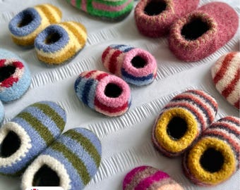 Puede incluir: Una colección de coloridas zapatillas de lana hechas a mano en varios patrones de rayas. Las zapatillas tienen una punta redondeada y un interior contrastante, con colores como rosa, verde, azul, amarillo y rojo. Dispuestas sobre una superficie blanca texturizada.