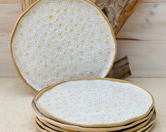 May include: A set of six white ceramic dinner plates with a daisy pattern and yellow centers. The plates have a slightly raised rim and a rustic, handmade look.