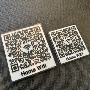 May include: Two white square signs with black QR codes and the text "Home Wifi" printed on them. The signs are on a black textured surface.