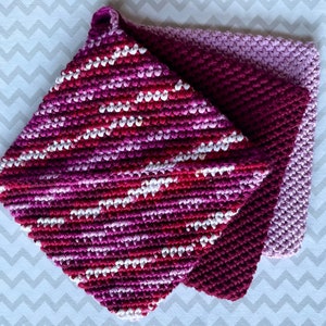 Può includere: Tre presine all'uncinetto in tonalità di rosa, viola e bianco. Le presine sono realizzate con un punto a trama e hanno una forma quadrata.