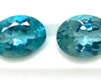 Coppia di pietre preziose sciolte, ovali e sfaccettate, di apatite verde naturale, ideali per la creazione di gioielli.