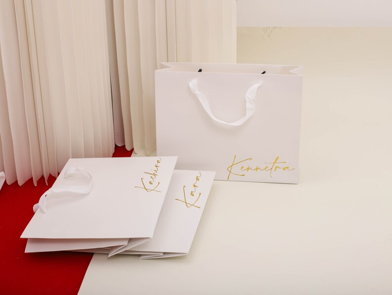 May include: Two white paper shopping bags with gold lettering. The bag on the left says "Kachira" and the bag on the right says "Kennetora".