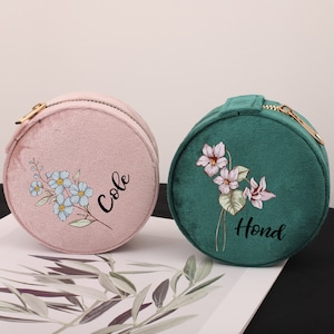 Puede incluir: Dos cajas redondas de joyería de terciopelo con diseños florales y nombres personalizados. La caja rosa tiene un diseño floral azul y el nombre "Cole" escrito en ella. La caja verde tiene un diseño floral rosa y el nombre "Hond" escrito en ella.