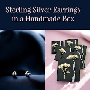May include: Sterling silver earrings in a handmade box with a pressed flower design. The earrings are small and delicate, and the box is black with a white border.