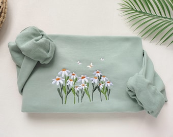 May include: A light green sweatshirt with embroidered white daisies and butterflies. The sweatshirt has a ribbed cuff and hem.