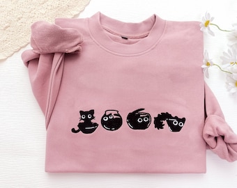 May include: A pink sweatshirt with a black embroidered design of five cats and fish bowls. The cats are all looking at the viewer with big eyes.