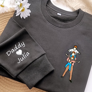 Puede incluir: Sudadera negra con un diseño bordado en blanco en la manga que dice "Daddy Julia" con un corazón. La parte delantera de la sudadera tiene un diseño bordado de un padre y tres hijos.