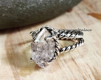 May include: A silver ring with a clear quartz crystal set in a twisted band. The ring is on a wooden surface.
